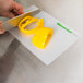 A person slicing a yellow bell pepper on a WebstaurantStore flexible cutting board.