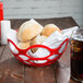 A close up of a red open weave basket filled with rolls on a table.