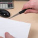 A hand using a Westcott 8" Letter Opener with a serrated stainless steel blade to open a white envelope.
