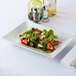 A plate of salad with strawberries and cheese on a white rectangular porcelain platter.