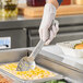 A hand in a glove holding a Vollrath Jacob's Pride slotted spoon scooping food.