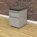 A grey file cabinet with a cushion on top.