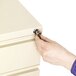 A hand using a key to open a drawer with an Alera chrome metal pedestal file lock core inside.