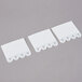 Three white plastic 3M Command picture hanging strips on a white paper background.