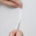 Hands holding a 3M Command White Picture Hanging Strip on a white wall.