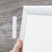 A hand holding a white frame next to a piece of white Scotch multi-purpose fastener tape.