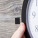 A hand holding a black clock with a 3M Scotch black fabric fastener set on the back.