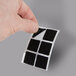 A hand holding a black square sticker with four squares on it.