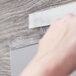 A hand using a white 3M Scotch clear fastener tape to cover a wood surface.