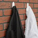 Two white 3M Command Designer Hooks holding black and white coats on a brick wall.