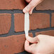 A person using a 3M Command white plastic strip to hang something on a white wall.