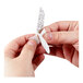 A person peeling the adhesive backing off a white 3M Command large wire hook.