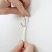 A person using a white 3M Command small wire hook to hang a white paper strip.