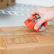 A hand using a 3M Scotch tape dispenser to tape a box.