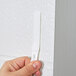 A hand holding a white 3M Command picture hanging strip.