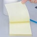 A hand holding a 3M Canary Yellow lined super sticky note pad with a pen.