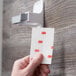 A hand holding a clear plastic strip with red text that says "3M Scotch"