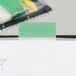 A close-up of a green Post-It page flag attached to a clipboard.