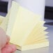 A hand holding a stack of yellow 3M Super Sticky fan-folded note pads.