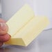 A hand holding a small yellow 3M Post-It note pad.