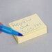 A person writing with a blue pen on a 3M Canary Yellow Post-It note.