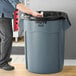 A man standing next to a Rubbermaid Brute 55 gallon gray round trash can.
