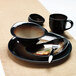 A close-up of a black bowl on a table setting with a plate and silverware.