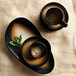 A black and brown Libbey Pebblebrook porcelain saucer with a cup on a table.