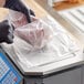 A person in black gloves using a Choice unprinted plastic deli saddle bag to weigh meat.