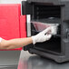 A person in a glove putting a foil container into a red Metro MLC1 Mightylite Pan Carrier.