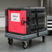 A black and red Metro Mightylite Pan Carrier Dolly carrying a black and red container.