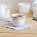 A close-up of a white Tuxton sake cup full of red liquid.