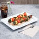 A white rectangular melamine serving platter with a plate of food and a drink on a table with a fork.