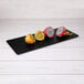 A group of cut fruit on a black rectangular serving board.