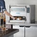 A woman using a TurboChef countertop ventless oven to cook food.