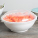 A clear plastic catering bowl lid on a bowl of carrots.