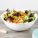 A white high profile plastic catering bowl filled with salad on a table.
