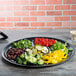 A black Fineline plastic catering tray with 7 compartments filled with broccoli and vegetables on a table.