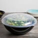 A black Fineline high profile plastic catering bowl filled with salad and covered with a clear lid.