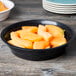 A black Fineline low profile plastic serving bowl filled with sliced fruit on a table.