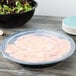 A black Fineline low profile plastic catering bowl filled with salad on a wood table.