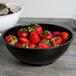 A black Fineline high profile plastic catering bowl filled with strawberries on a table with a bowl of salad.