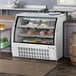 An Avantco white refrigerated deli case with a curved glass door full of food.