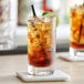 Two Acopa highball glasses of iced tea with lime and blackberries on a table.