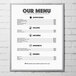 An Aarco aluminum slide frame with a white border displaying a menu with black text on a brick wall.