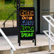 A black A-Frame sign with a black marker board displaying colorful writing on a sidewalk.