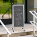 An Aarco aluminum A-Frame sign board with a slate gray chalkboard on a sidewalk.