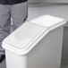 A person opening the lid of a white plastic bin.