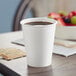 A white Solo paper hot cup on a table with a cup of coffee and fruit.