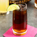 A Stolzle tumbler of brown liquid with a lime wedge on top of it.